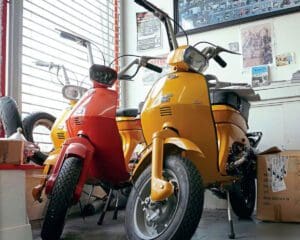 Three Luna scooters, 2 yellow and 1 red, in the front of the store by a window