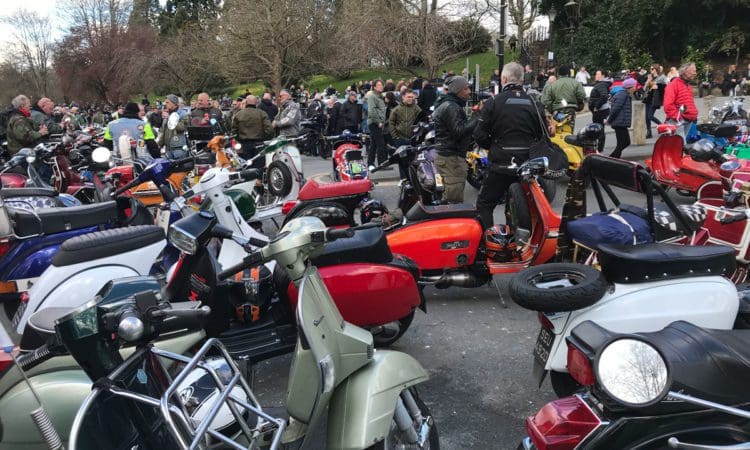 Loads of scooters with people stood in the background talking